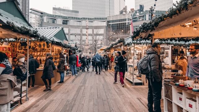 Groups of people move through a bright looking Christmas market with lots of lights and colourful decorations.