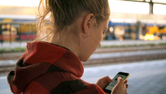 A woman walks with her phone in front of her on a city street.