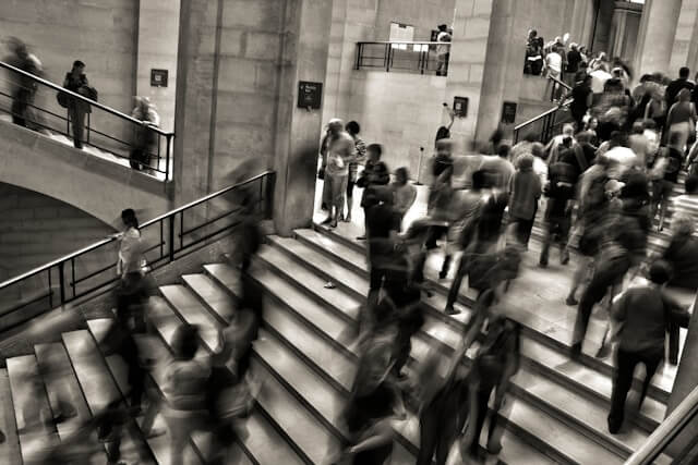 Black and white blurred photo of a crowd of people walking different directions on a staircase.