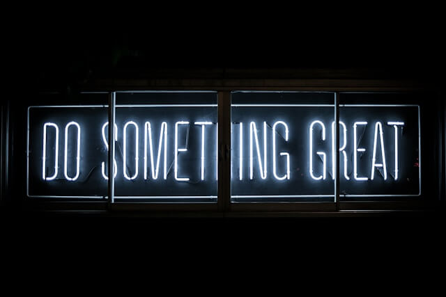 A blue neon sign on a black background says DO SOMETHING GREAT.