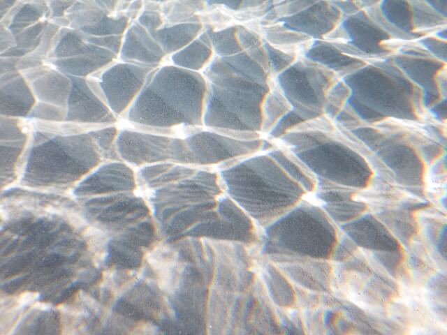 Waves reflect shimmering light from the sun onto the sand of the ocean floor.