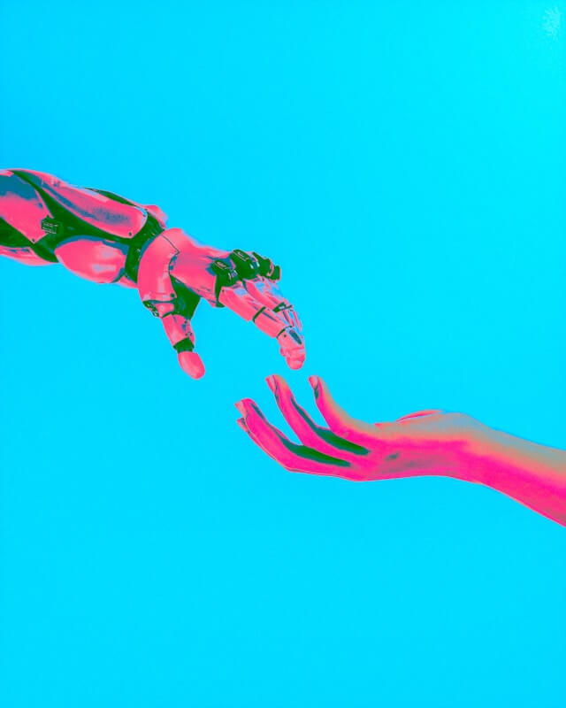 A neon pink robot hand reaches for a neon pink human hand.