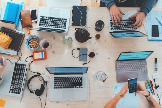 Top down photo of a group of people working on their laptops around a table.